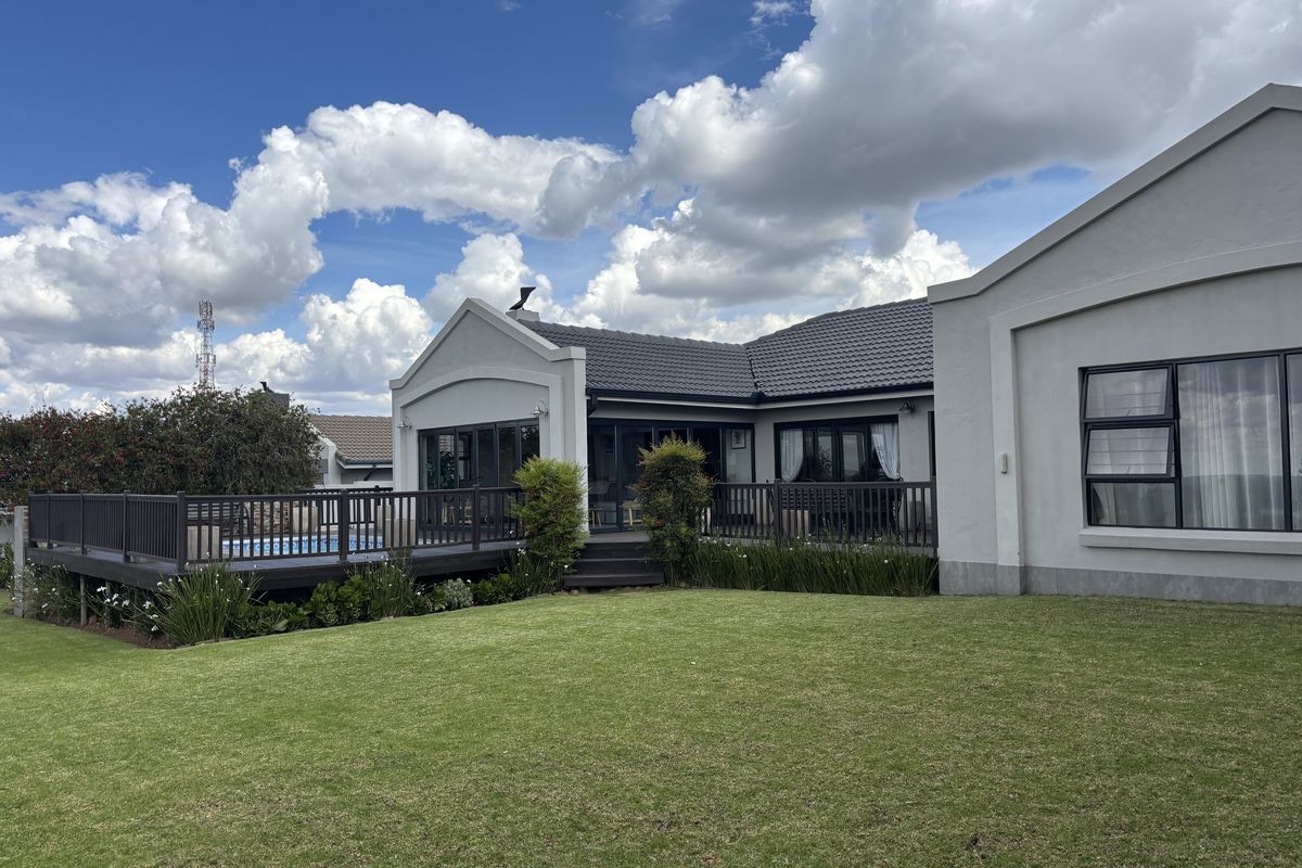 A well-maintained rear exterior view featuring a spacious raised timber deck, a swimming pool, and a neatly landscaped lawn against the house facade.
