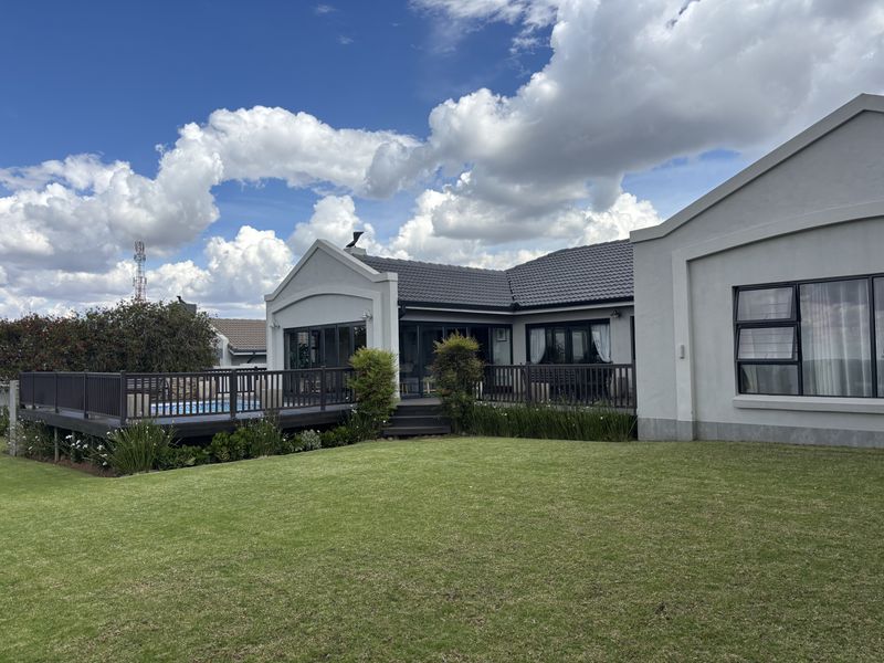 A well-maintained rear exterior view featuring a spacious raised timber deck, a swimming pool, and a neatly landscaped lawn against the house facade.