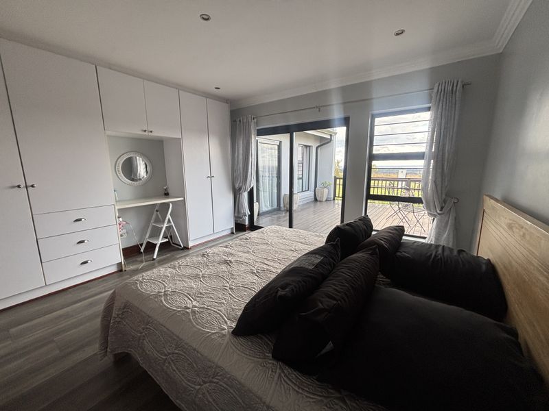 Spacious bedroom featuring extensive built-in cabinetry, modern laminate flooring, and sliding glass doors providing direct access to an outdoor balcony area.