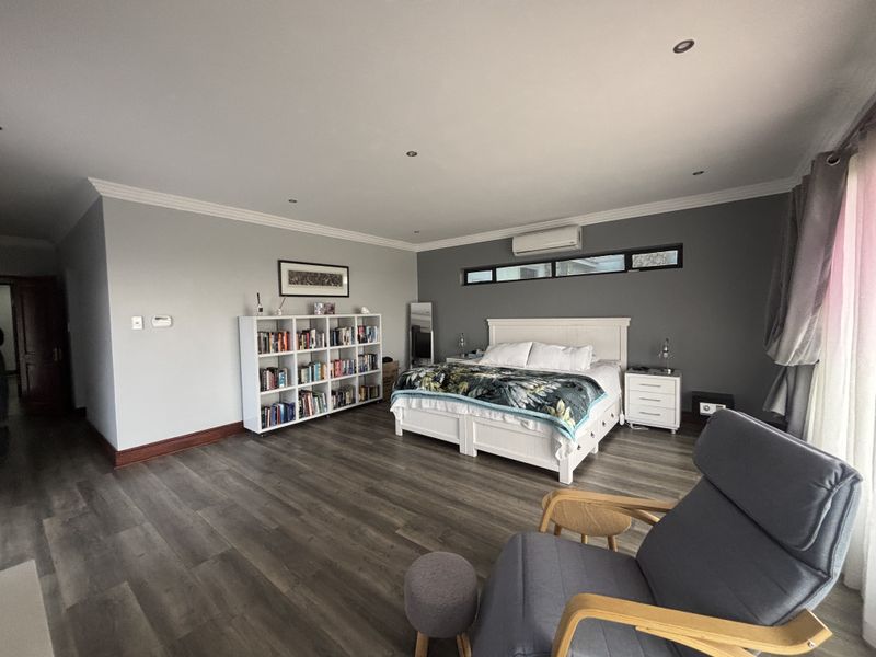 Spacious bedroom featuring modern laminate flooring, recessed downlighting, crown molding, and a wall-mounted split-system air conditioner.