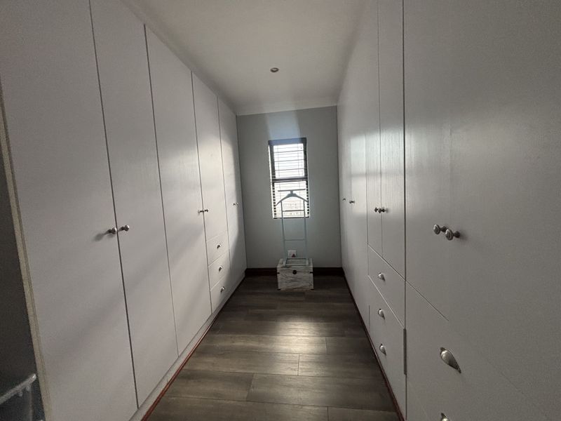 A clean and modern walk-in closet or dressing area featuring extensive floor-to-ceiling built-in cabinetry and durable laminate flooring.