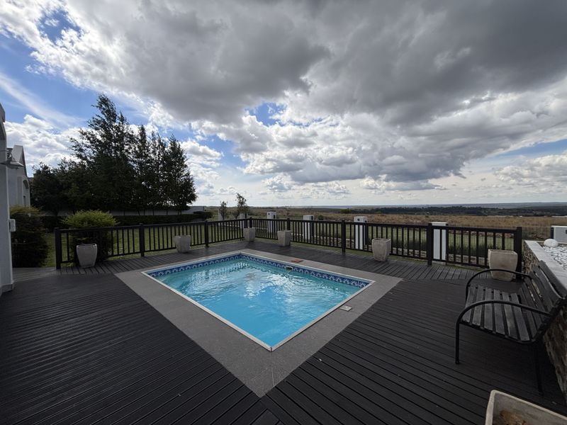 A well-maintained outdoor pool area featuring timber decking, stone coping, and perimeter railing, offering expansive views of the surrounding landscape.