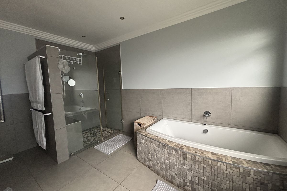 A modern bathroom featuring a built-in bathtub with mosaic tile detailing, a separate glass-enclosed shower, and neutral large-format floor and wall tiles.