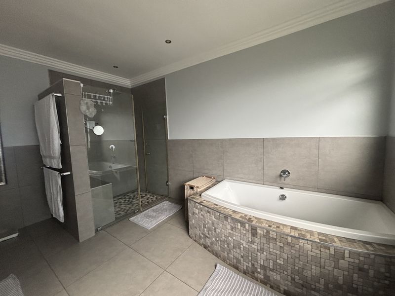 A modern bathroom featuring a built-in bathtub with mosaic tile detailing, a separate glass-enclosed shower, and neutral large-format floor and wall tiles.