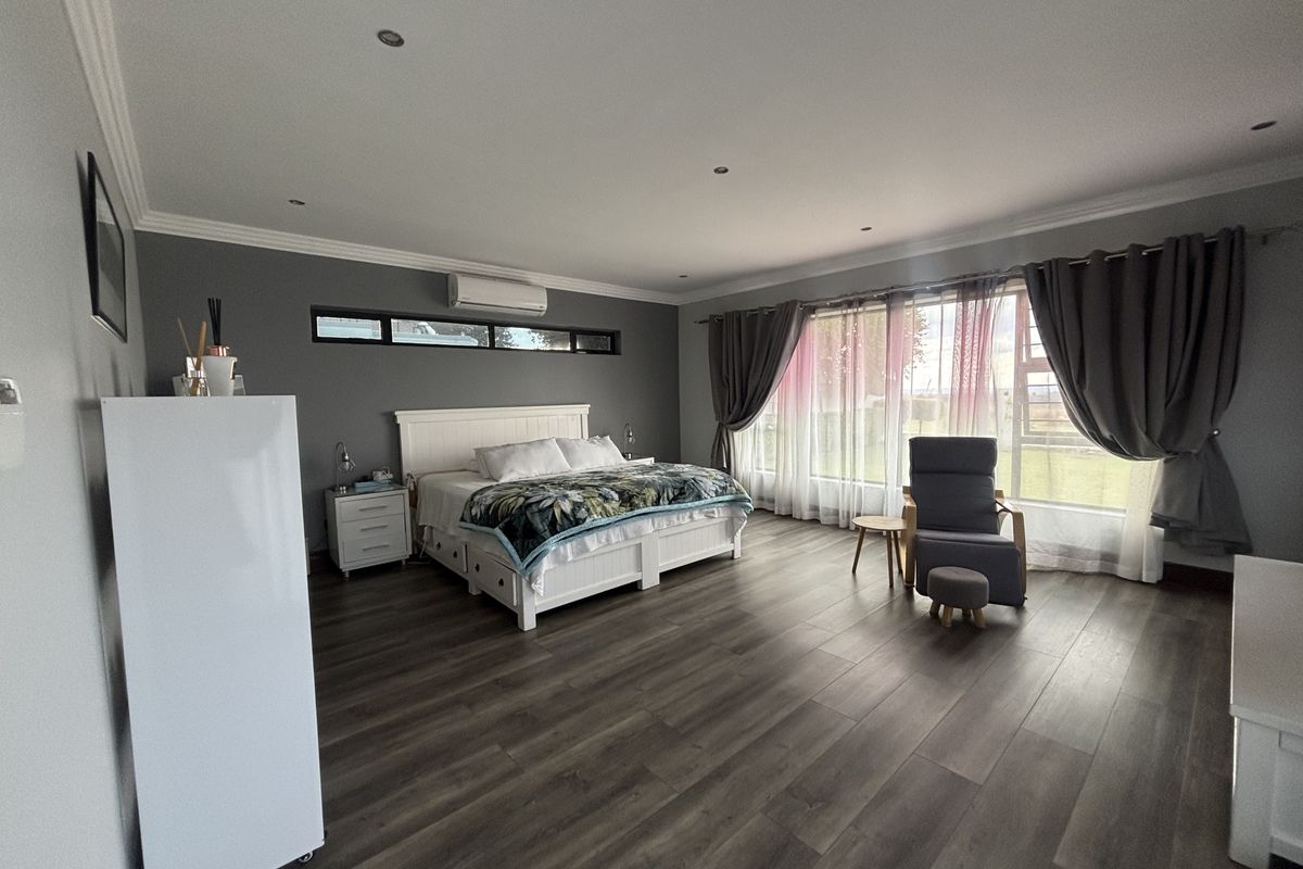 Spacious bedroom featuring modern laminate flooring, recessed downlighting, and a wall-mounted split-system air conditioner, offering a clean and well-maintained living environment.