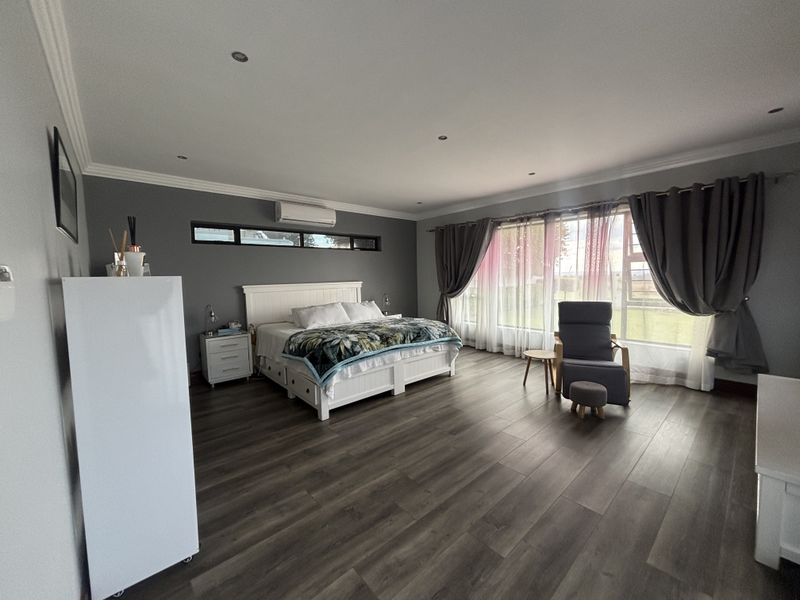 Spacious bedroom featuring modern laminate flooring, recessed downlighting, and a wall-mounted split-system air conditioner, offering a clean and well-maintained living environment.