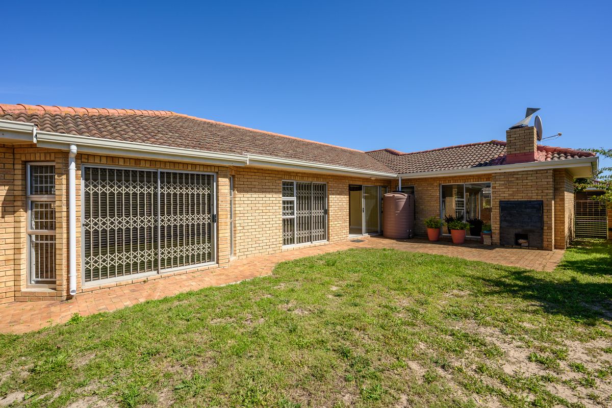 Rear view of the townhouse featuring a paved patio area, built-in braai, and direct access to the garden through sliding doors with security gates.