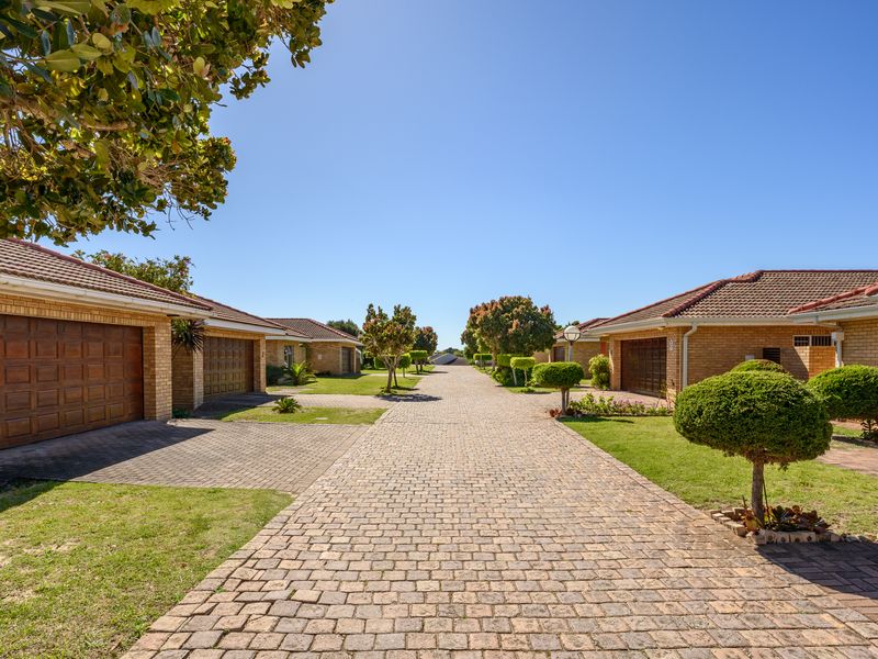 A well-maintained townhouse complex featuring a central brick-paved driveway, facebrick facades, and neat landscaped gardens under a clear blue sky.