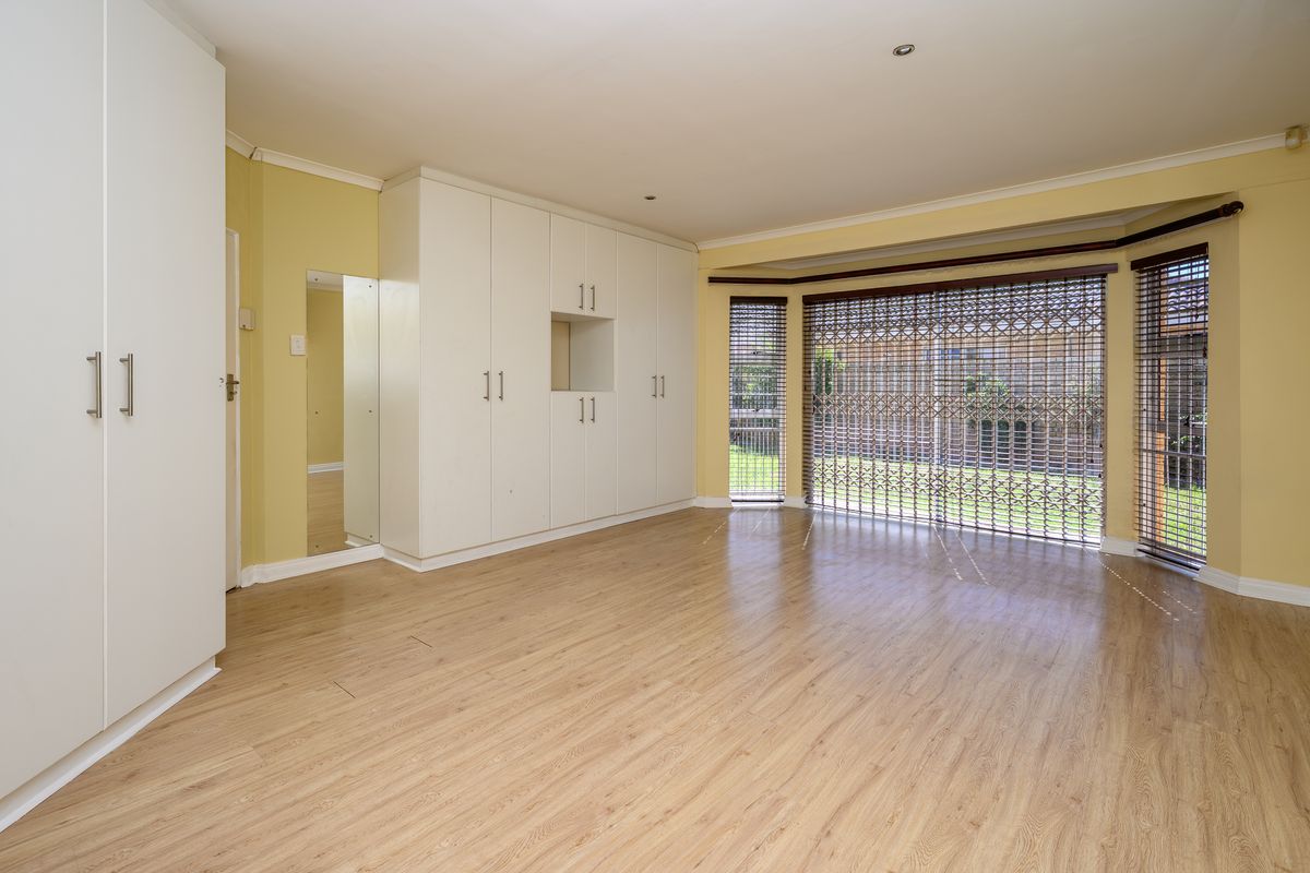 Spacious bedroom featuring light laminate flooring, extensive built-in cupboards, and large windows with security gates, offering a bright and functional living space.