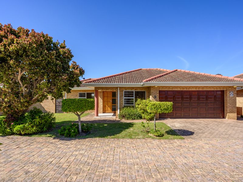 Front elevation of a brick townhouse featuring a tiled roof, paved driveway, and an integrated double garage with a timber door.