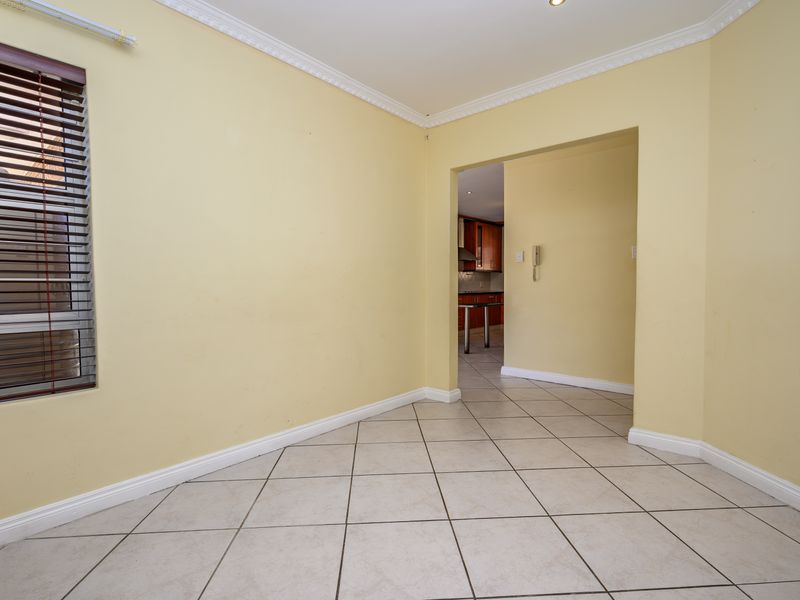 An empty living area featuring neutral yellow walls, tiled flooring, crown molding, and a view through to the kitchen area.