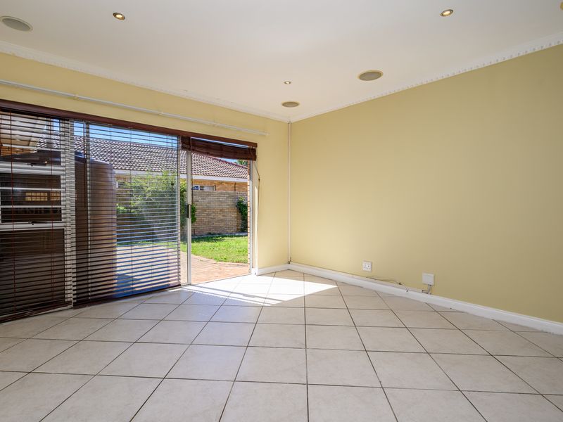 A bright, empty living room featuring tiled flooring, recessed lighting, and a large sliding glass door providing direct access to the rear garden.