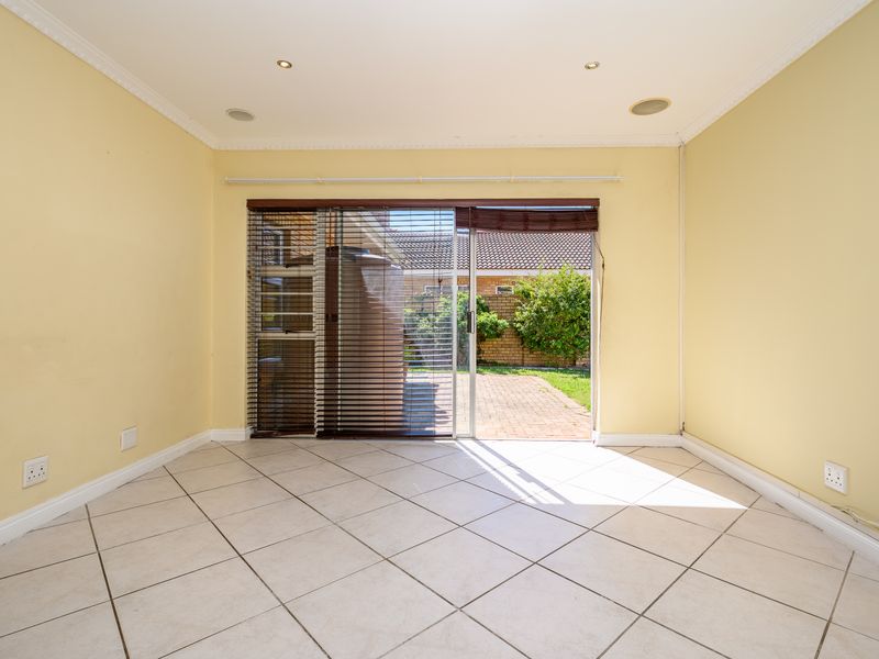 An empty, light-filled living room featuring neutral tiled flooring, recessed downlights, and a large sliding glass door providing direct access to the rear patio.