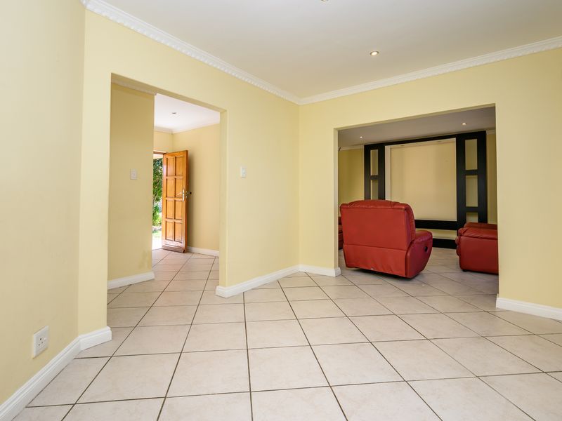 Spacious living area featuring neutral tiled flooring, crown molding, and a built-in shelving unit, providing a versatile layout with easy access to the entrance.