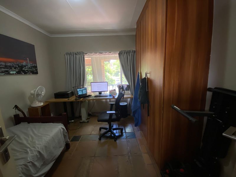A bedroom featuring built-in wooden wardrobes, tiled flooring, and a window with natural light, suitable for use as a bedroom or home office.