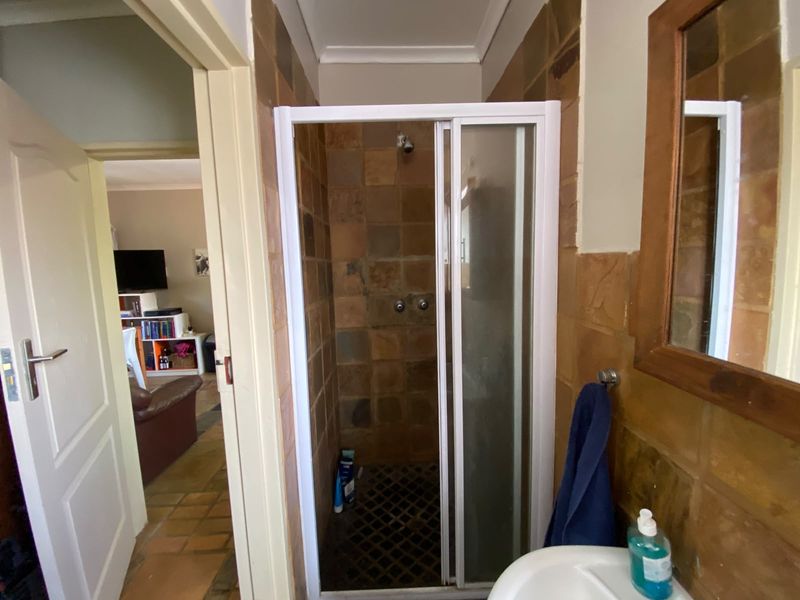 A functional bathroom featuring a shower enclosure with tiled walls and a pedestal basin, showing signs of age and wear.