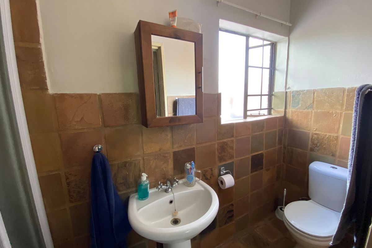 A compact bathroom featuring a pedestal basin, toilet, and dated natural stone-style wall tiles with a window providing natural light.