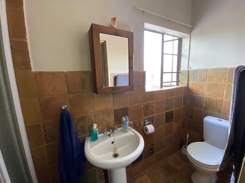 A compact bathroom featuring a pedestal basin, toilet, and dated natural stone-style wall tiles with a window providing natural light.