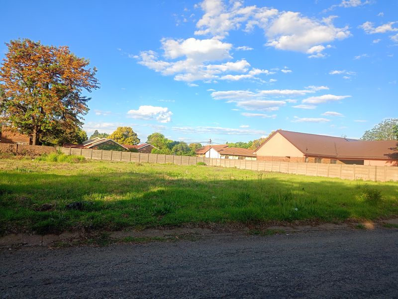 A vacant residential plot featuring a level grassed surface and enclosed by a precast concrete boundary wall in a suburban setting.