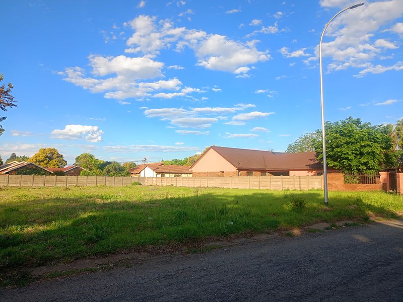 A vacant residential plot featuring a precast concrete boundary wall, street lighting, and direct access to an asphalt road.
