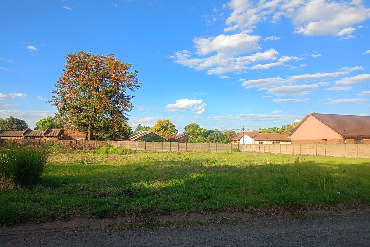 A vacant residential plot featuring a grassy surface, enclosed by a precast concrete boundary wall with a mature tree on the property.