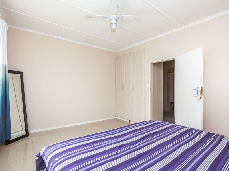 A bedroom featuring tiled flooring, built-in cupboards, and a ceiling fan, offering a functional space with neutral wall finishes.