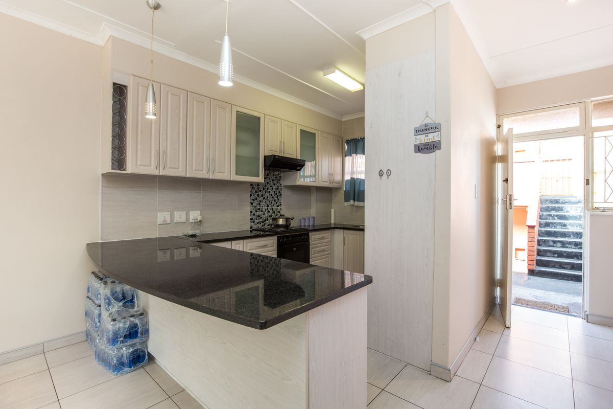 A well-maintained kitchen featuring granite countertops, built-in cabinetry, a mosaic tile backsplash, and ceramic tile flooring, with direct access to an exterior entrance.