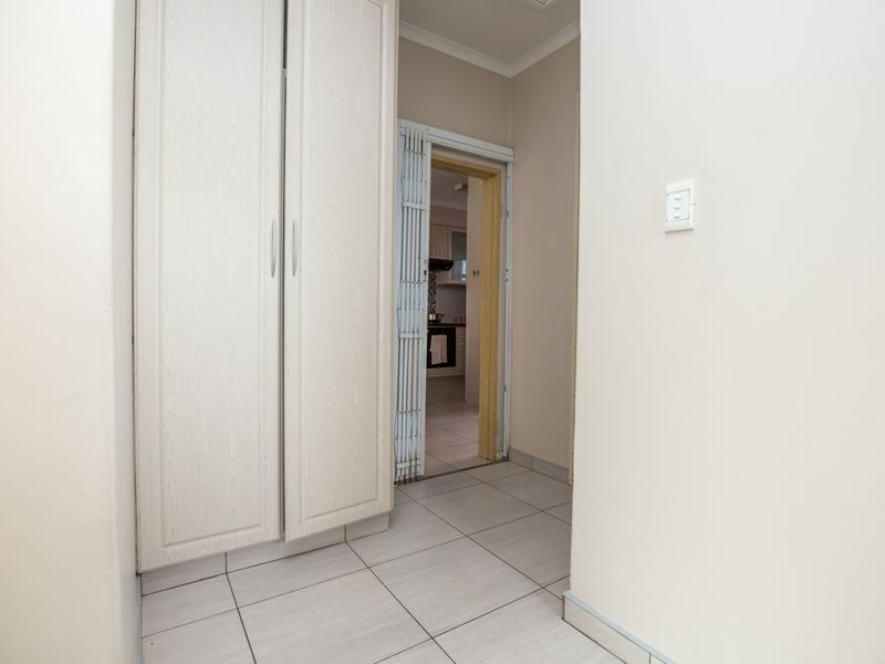 A clean hallway featuring neutral tiled flooring and built-in storage cupboards, providing access to the kitchen area through a security gate.