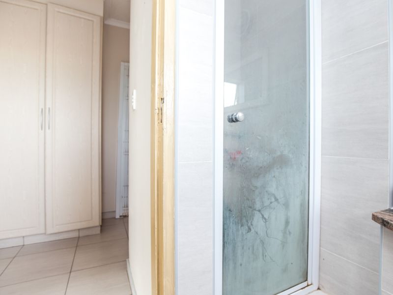 Bathroom featuring a shower enclosure with tiled walls and flooring, adjacent to a hallway with built-in cupboards.