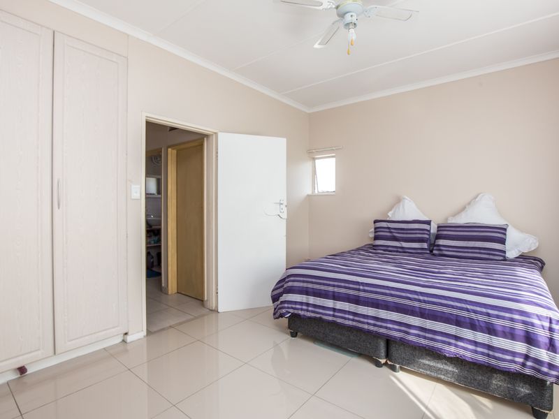A bedroom featuring built-in cupboards, tiled flooring, and a ceiling fan, with an adjoining doorway leading to another room.