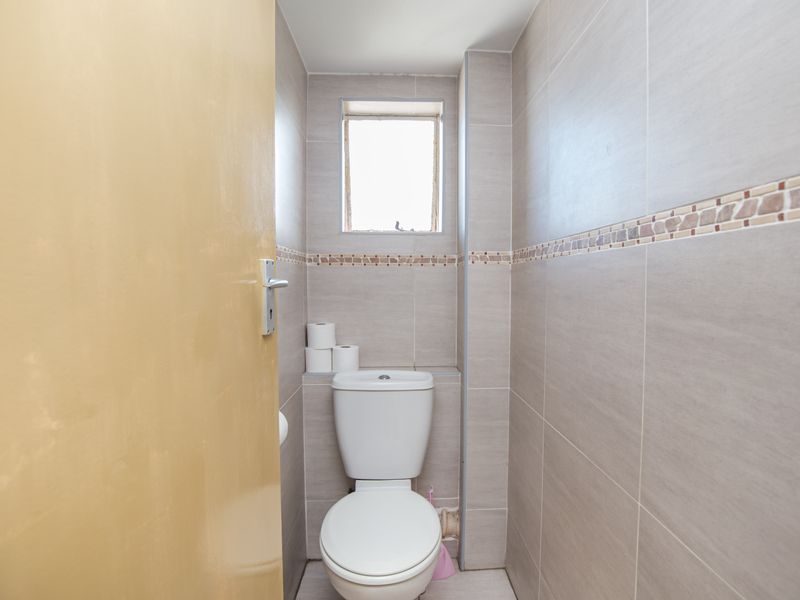 A compact bathroom featuring neutral wall tiles, a standard toilet, and a small window for natural light.