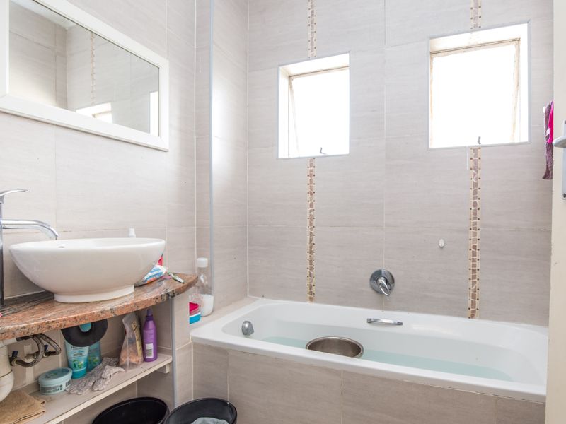 A functional bathroom featuring a vessel sink on a granite vanity, a built-in bathtub, and neutral wall tiling with decorative accents.