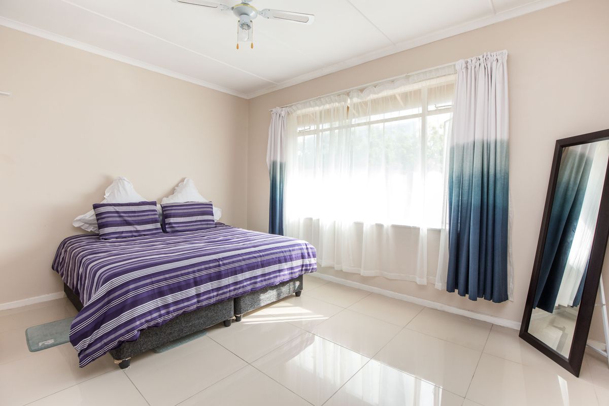 A bright bedroom featuring neutral walls, large windows with natural light, and clean tiled flooring throughout.