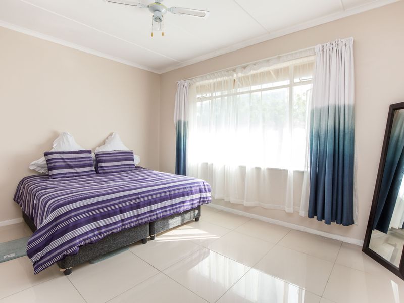 A bright bedroom featuring neutral walls, large windows with natural light, and clean tiled flooring throughout.