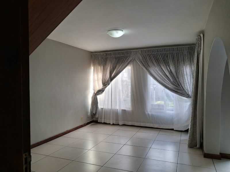 A bright, empty living room featuring neutral tiled flooring and a distinctive architectural archway, offering a clean canvas for interior design.