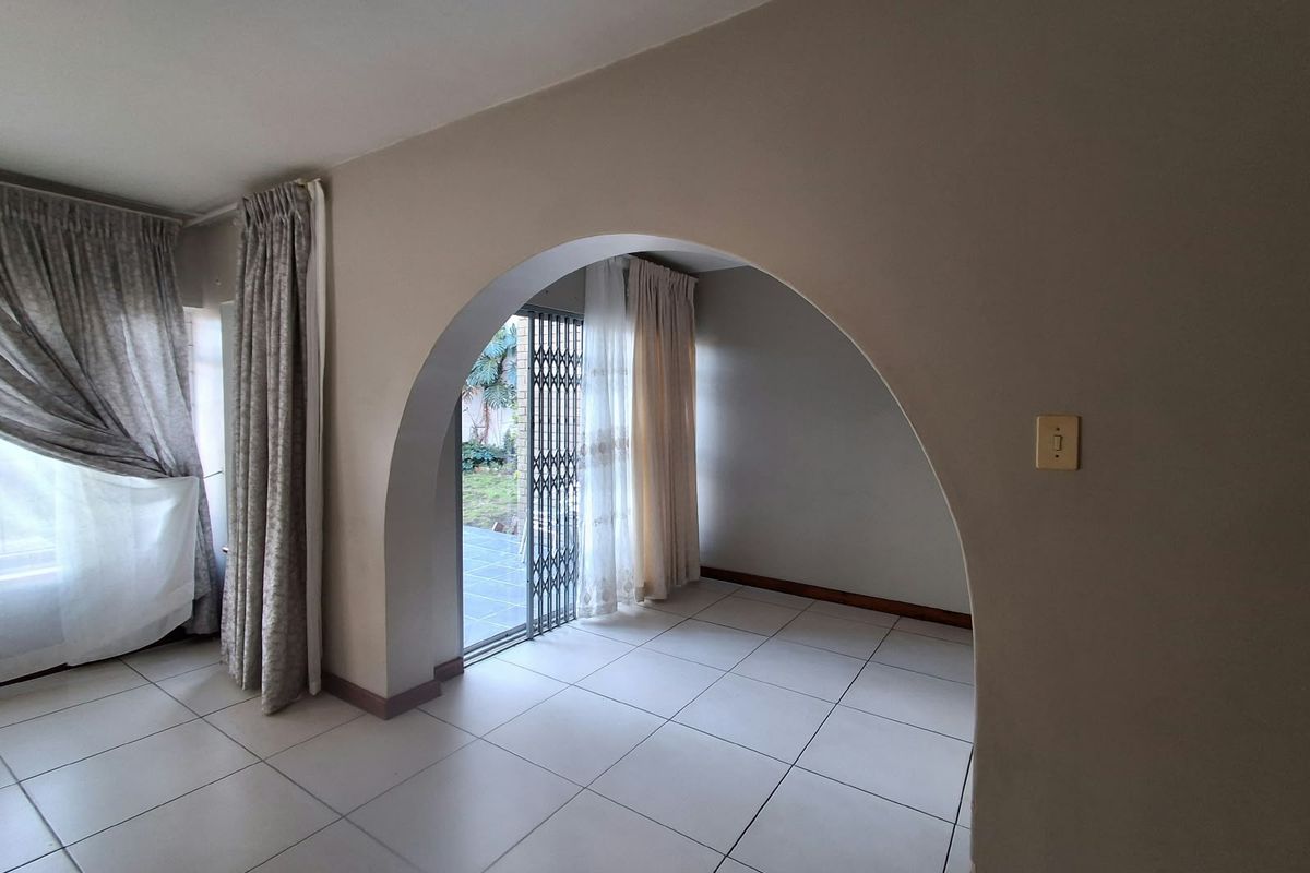 An empty living area featuring neutral tiled flooring, a distinctive architectural archway, and direct access to an outdoor patio through a security gate.