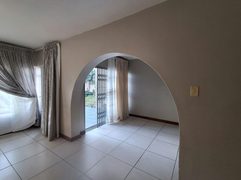 An empty living area featuring neutral tiled flooring, a distinctive architectural archway, and direct access to an outdoor patio through a security gate.