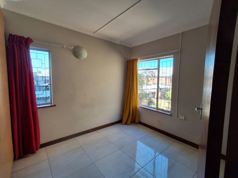 An empty bedroom featuring tiled flooring, neutral wall paint, and windows fitted with security bars.