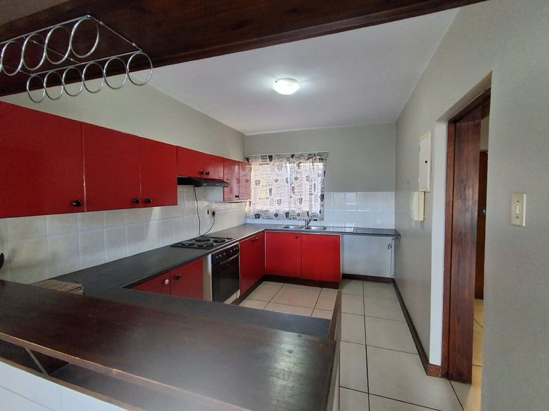 Functional kitchen featuring red cabinetry, dark countertops, built-in oven and hob, tiled backsplash, and a breakfast bar counter.