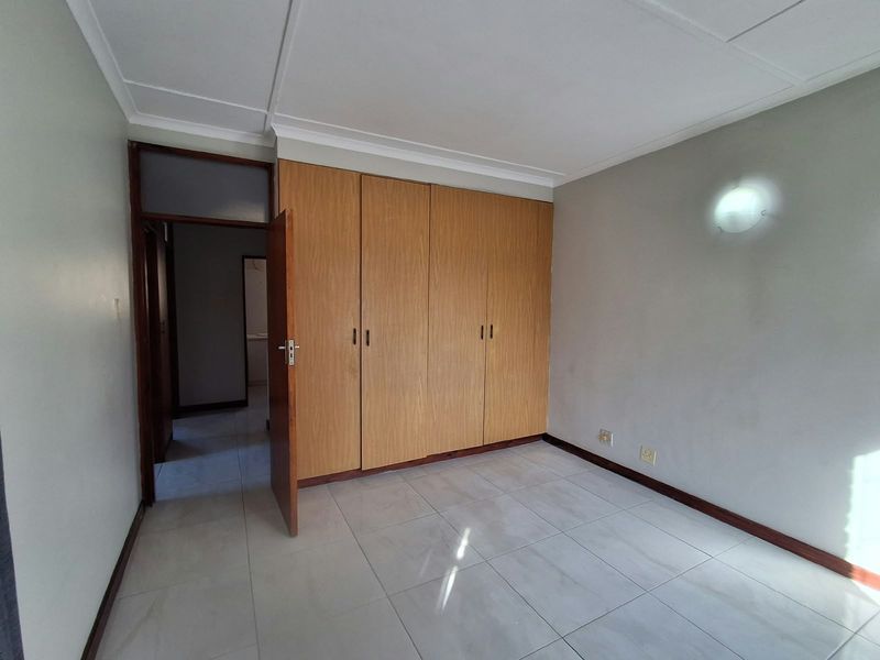 An empty bedroom featuring tiled flooring, coved ceilings, and built-in wooden cupboards, offering a clean and neutral space ready for personalization.