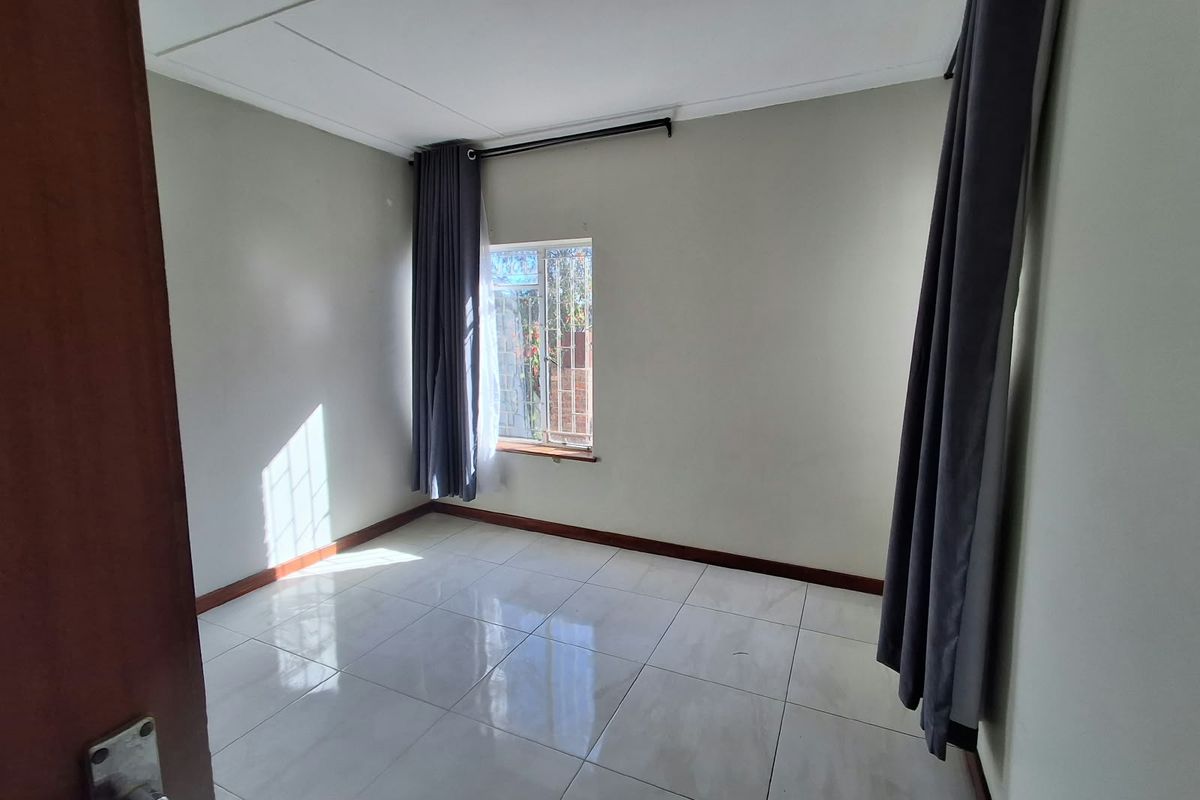 A bright, empty bedroom featuring neutral wall paint, polished floor tiles, and security bars on the window.
