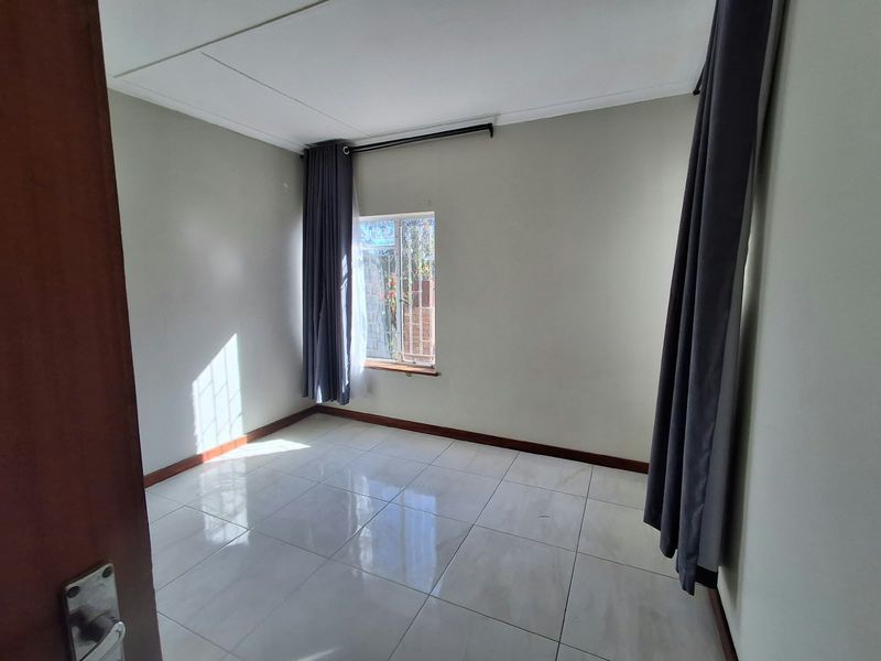 A bright, empty bedroom featuring neutral wall paint, polished floor tiles, and security bars on the window.