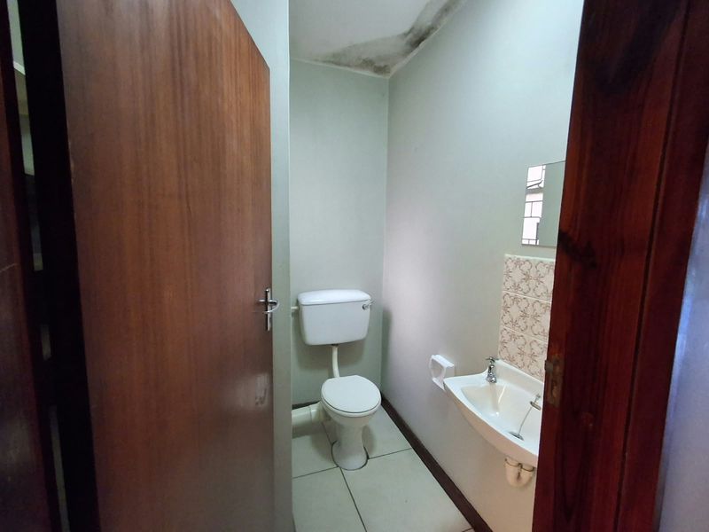 A compact guest bathroom featuring a toilet and wall-mounted basin, currently showing signs of water damage on the ceiling requiring repair.