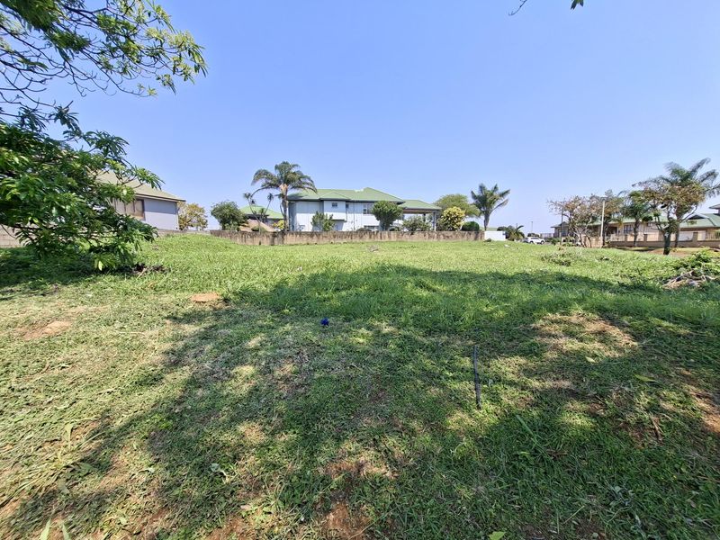 A vacant residential plot featuring a grass lawn and a perimeter retaining wall, situated in a developed neighborhood.