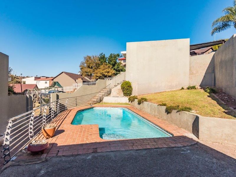 Outdoor pool area featuring a swimming pool with brick coping, concrete paving, and tiered retaining walls with metal safety railings.