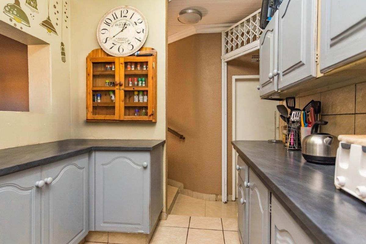 A functional kitchen area featuring grey cabinetry, dark laminate countertops, and tiled flooring, with a direct transition to an adjacent staircase.