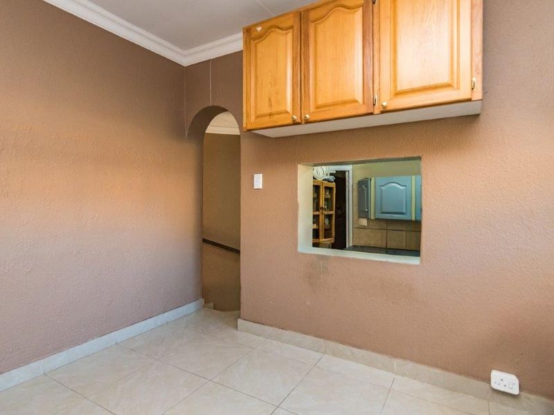 An empty living area featuring tiled floors, a decorative archway, and a serving hatch connecting to the kitchen with overhead wooden cabinetry.
