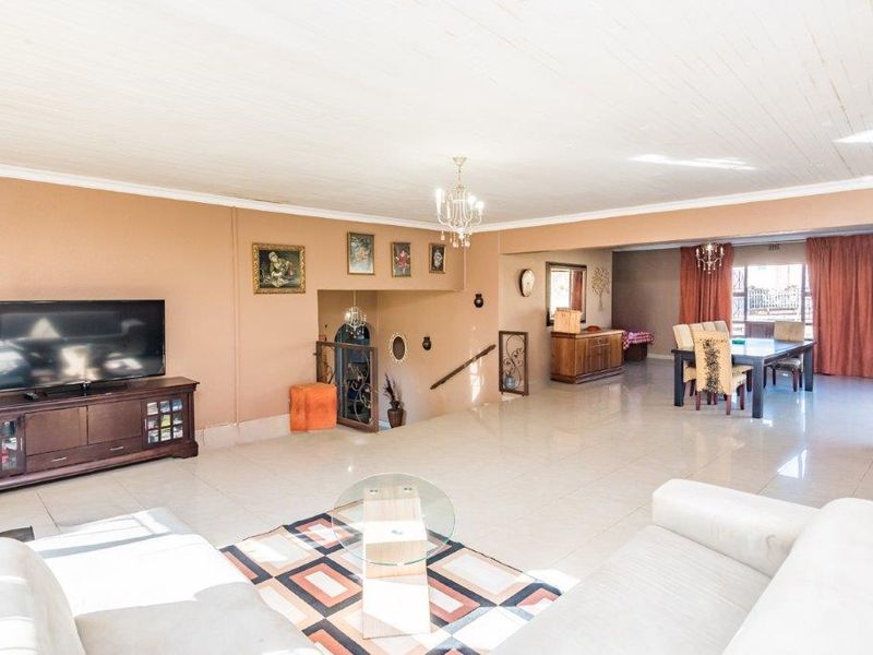 Spacious open-plan living and dining area featuring tiled flooring, a timber ceiling, and a wrought iron staircase leading to the lower level.
