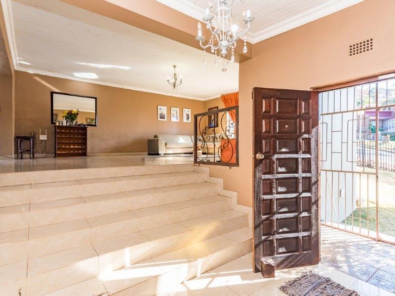 Spacious entrance hall featuring a tiled staircase leading to an open-plan living area, complete with a decorative chandelier and secure wrought iron gate.
