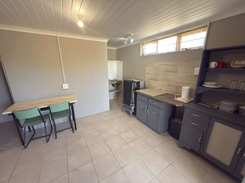 A functional kitchen area featuring tiled flooring, a tiled splashback, built-in cabinetry, and a sink, with a tongue and groove ceiling.